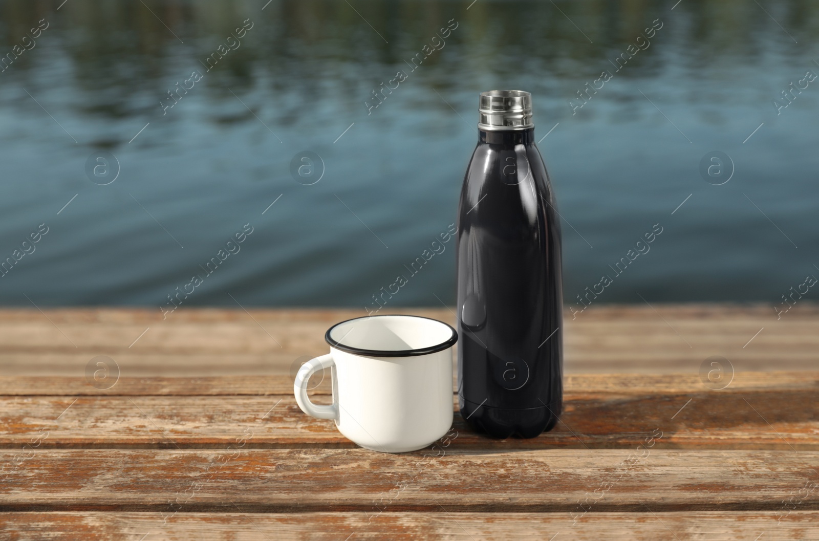 Photo of Modern black thermos bottle and cup on wooden surface near river