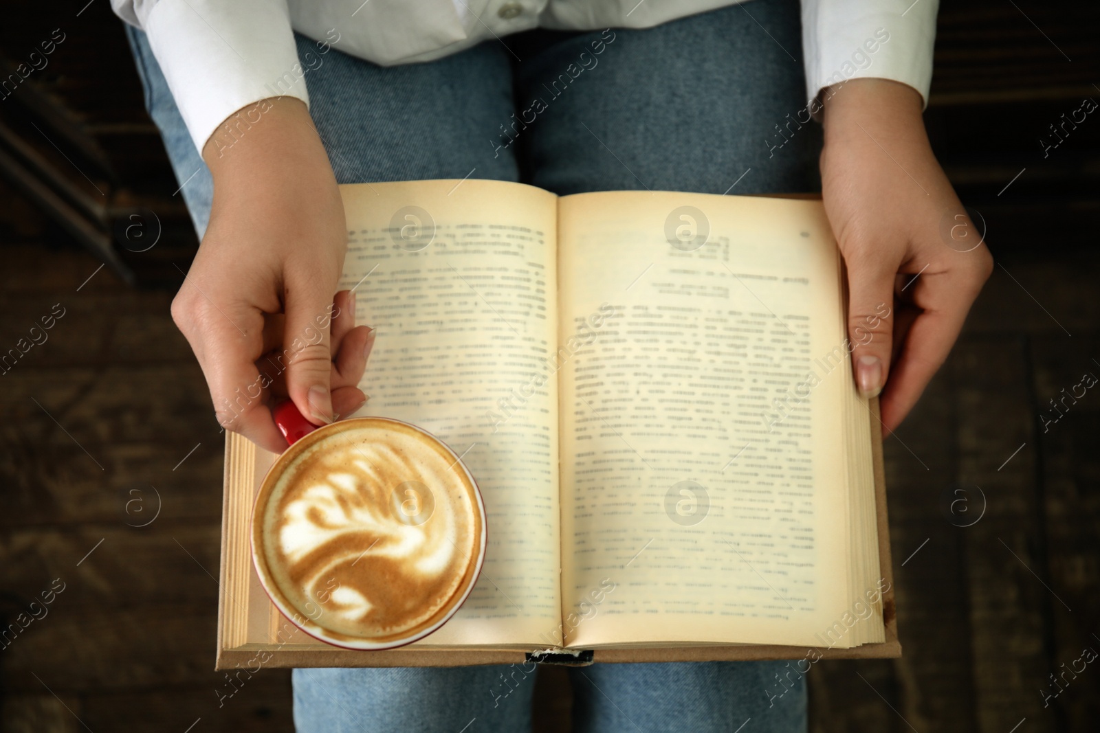 Photo of Woman with cup of coffee reading book indoors, top view