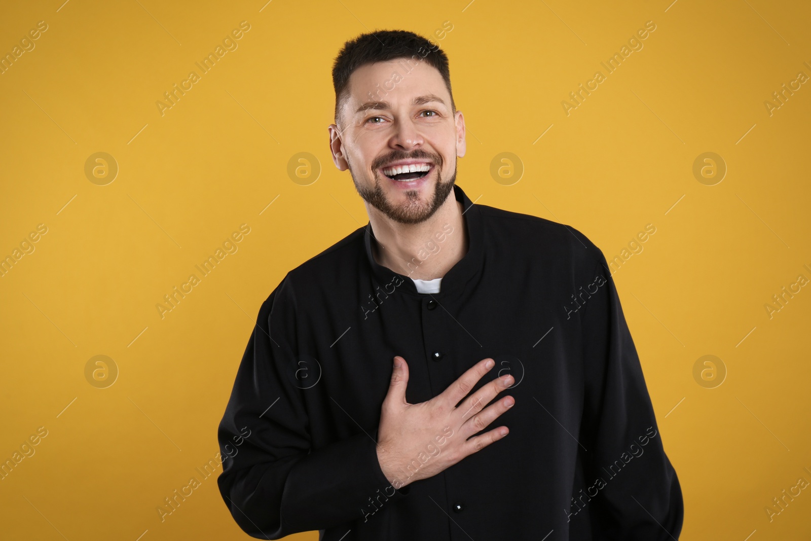 Photo of Priest wearing cassock with clerical collar on yellow background