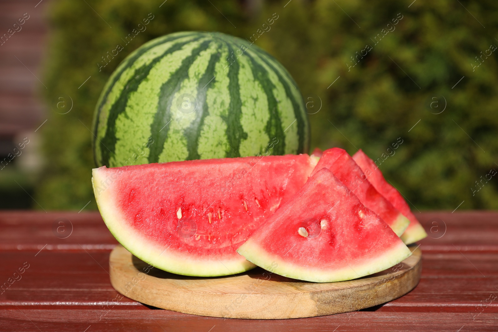 Photo of Delicious cut and whole ripe watermelons on wooden table outdoors