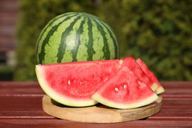 Photo of Delicious cut and whole ripe watermelons on wooden table outdoors