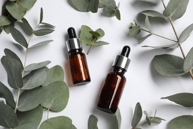 Photo of Aromatherapy. Bottles of essential oil and eucalyptus leaves on white background, flat lay