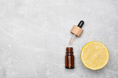 Bottle of essential oil with lemon slice on grey table, flat lay. Space for text