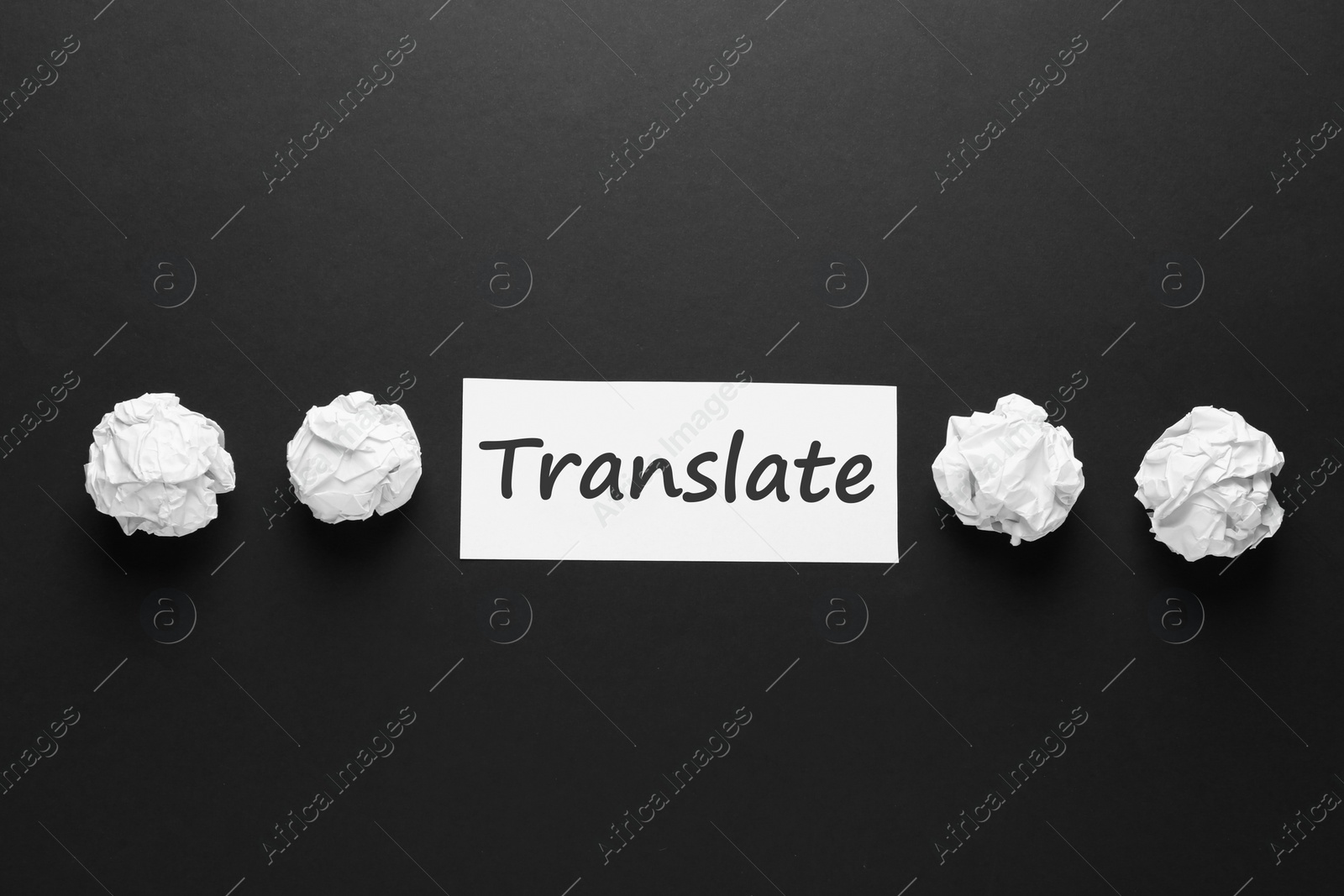 Photo of Card with word Translate and crumpled paper balls on black background, flat lay