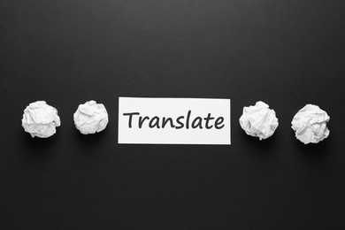 Photo of Card with word Translate and crumpled paper balls on black background, flat lay