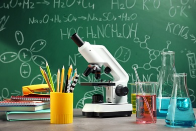 Photo of Laboratory glassware, microscope and stationery on table near chalkboard. Chemistry concept