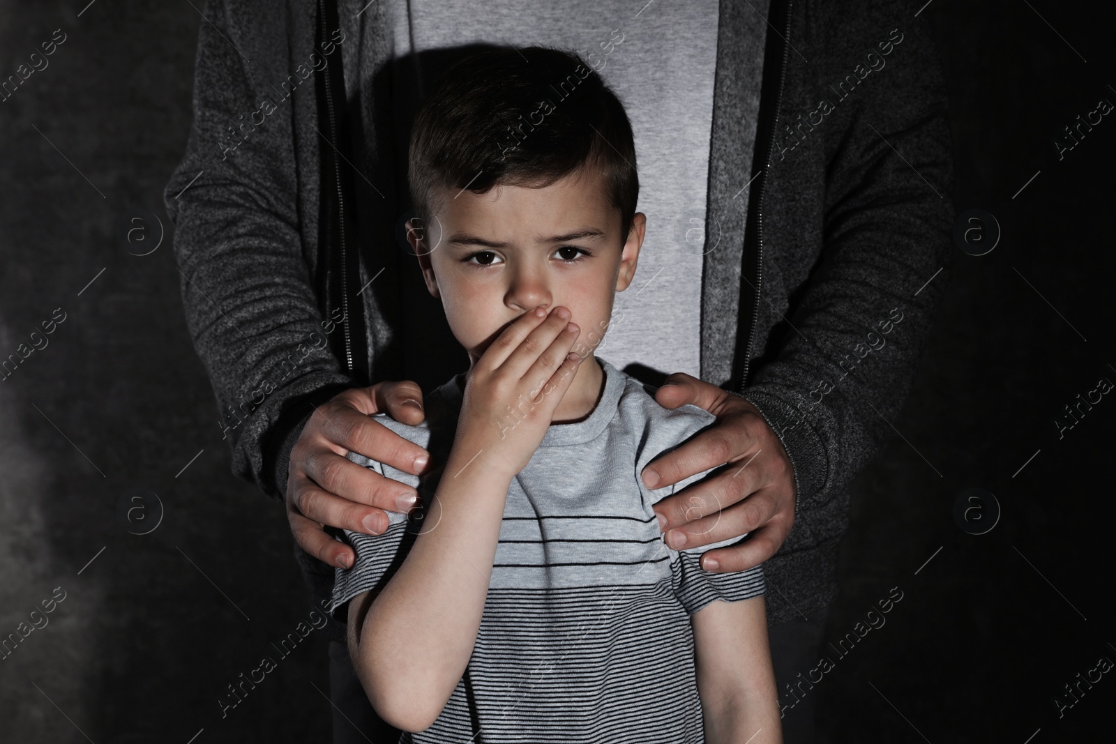 Photo of Scared little boy and adult man on dark background. Child in danger