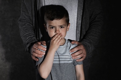 Scared little boy and adult man on dark background. Child in danger