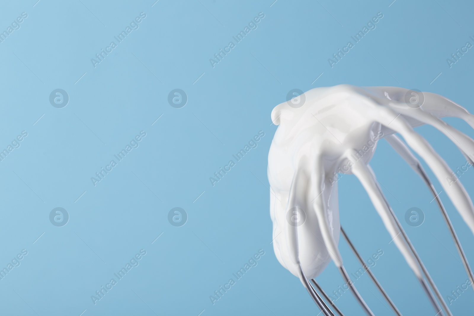 Photo of Whisk with whipped cream on light blue background, closeup. Space for text