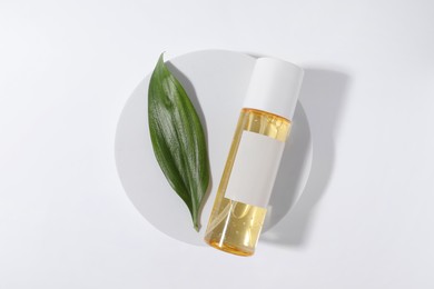 Photo of Bottle with cosmetic oil and green leaf on white background, top view