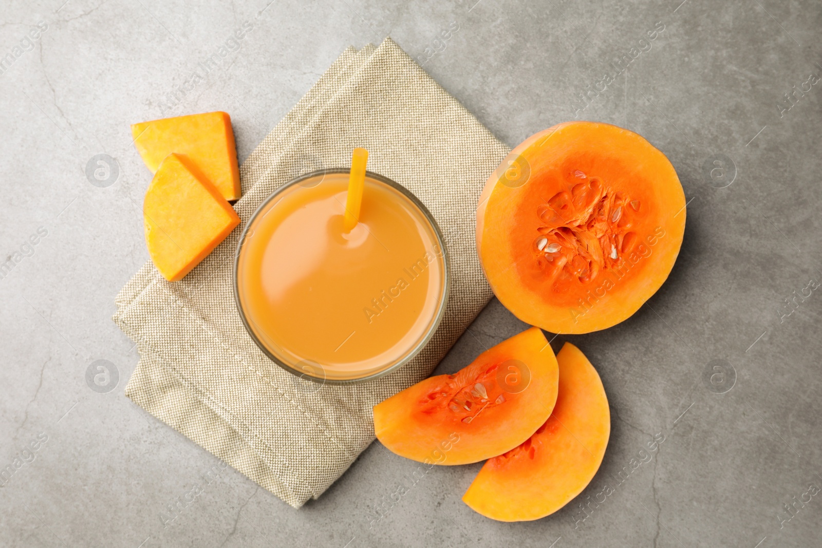 Photo of Tasty pumpkin juice in glass and cut pumpkin on light grey table, flat lay