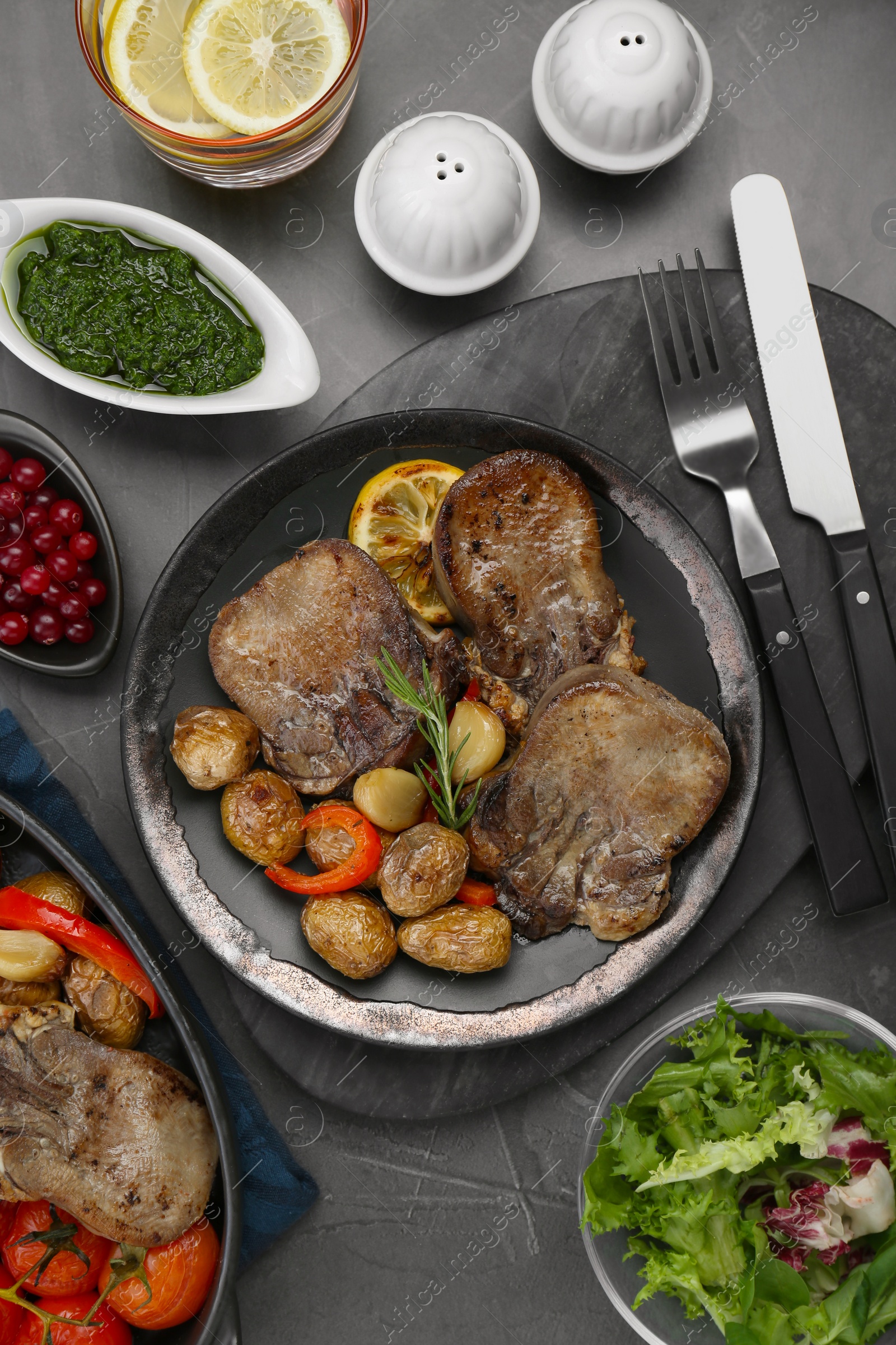 Photo of Tasty beef tongue pieces with potatoes and ingredients on grey table, flat lay