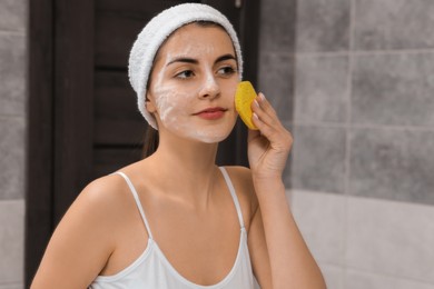 Photo of Young woman with headband washing her face using sponge in bathroom