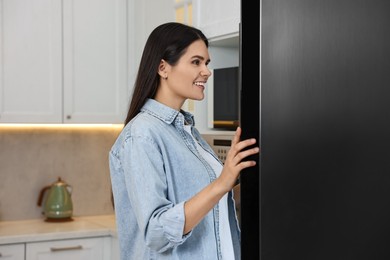 Young woman near modern refrigerator in kitchen