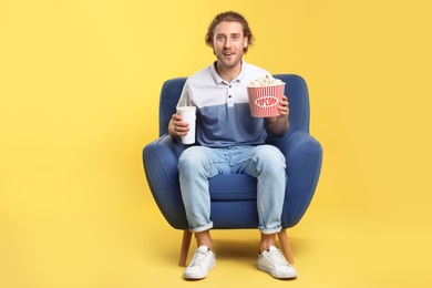 Photo of Emotional man with popcorn and beverage sitting in armchair during cinema show on color background