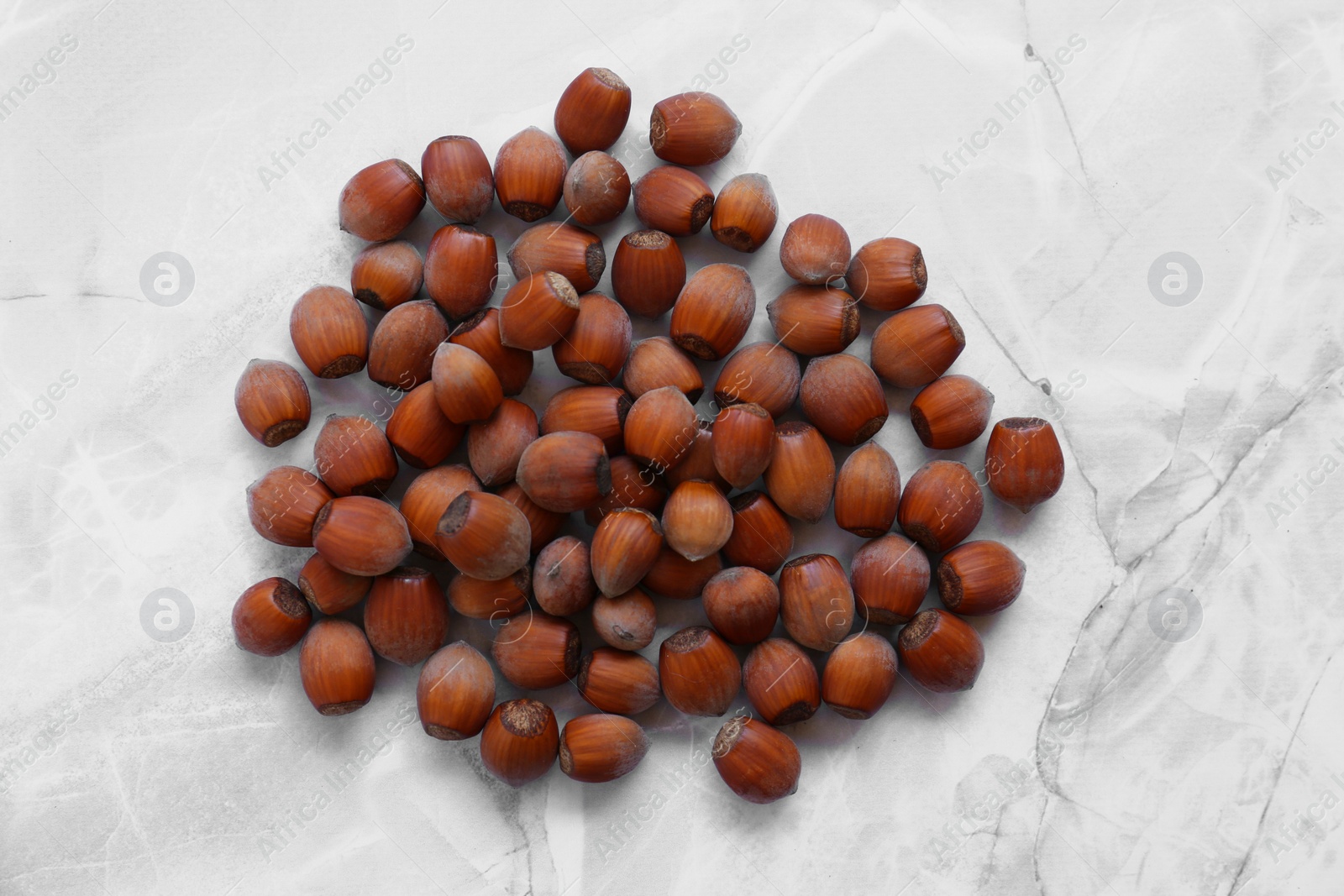 Photo of Pile of tasty hazelnuts on light marble table, top view