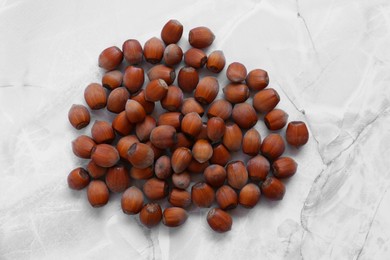 Photo of Pile of tasty hazelnuts on light marble table, top view