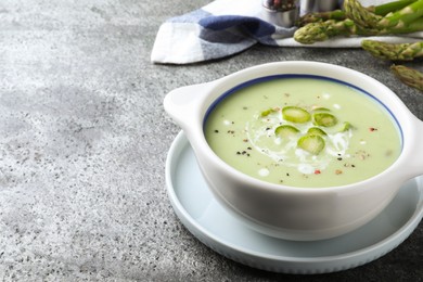 Photo of Bowl of delicious asparagus soup on grey table, space for text
