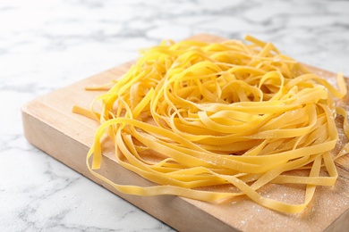 Photo of Wooden board with raw egg noodles on marble table, closeup