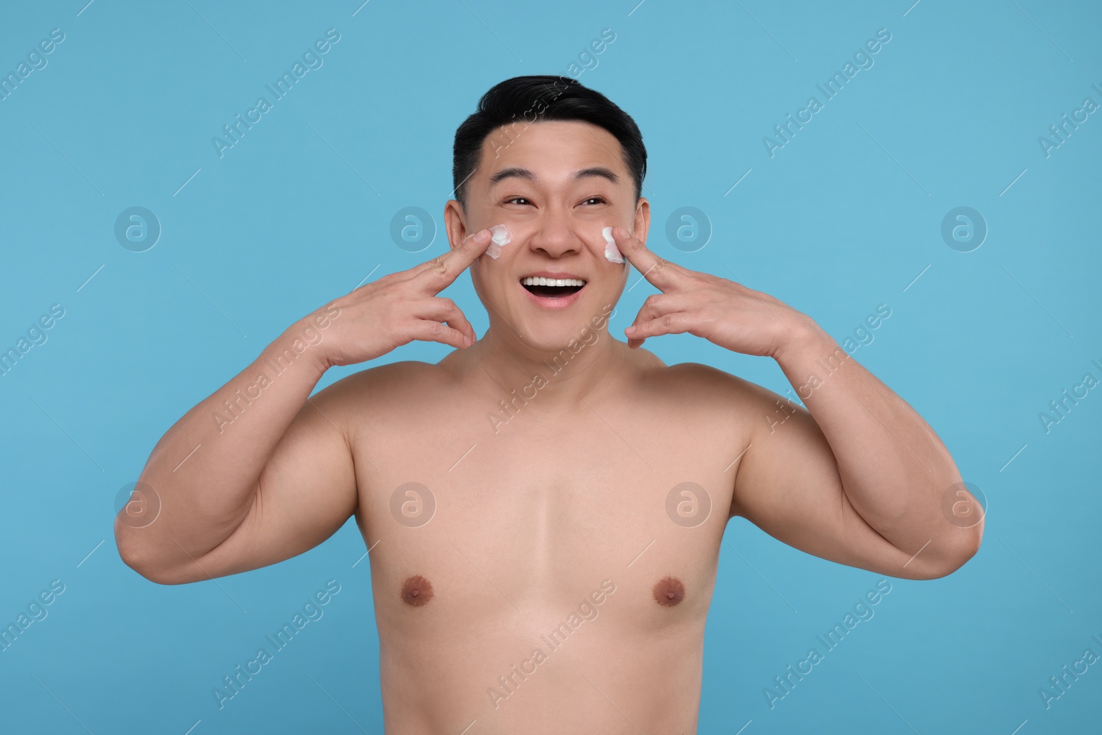 Photo of Happy man applying cream onto his face on light blue background