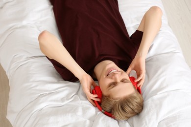 Photo of Teenage boy listening to music with headphones on bed, above view