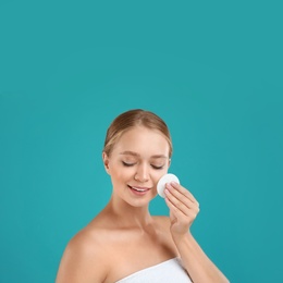 Photo of Beautiful young woman with cotton pad on turquoise background