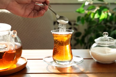 Woman adding sugar into aromatic tea at wooden table indoors, closeup