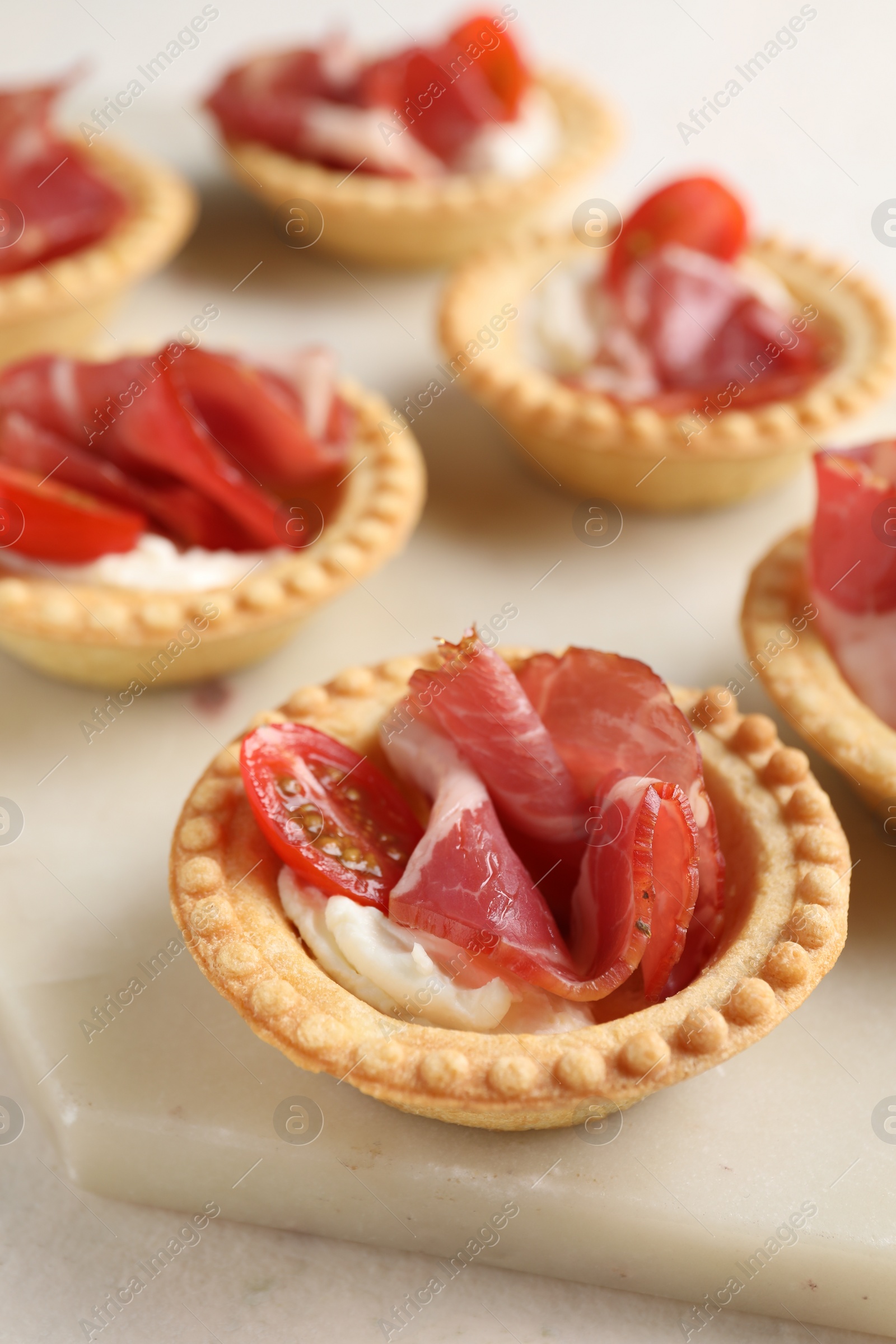 Photo of Delicious canapes with jamon, cream cheese and cherry tomatoes on light table, closeup