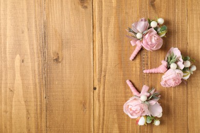 Photo of Stylish pink boutonnieres on wooden table, flat lay. Space for text