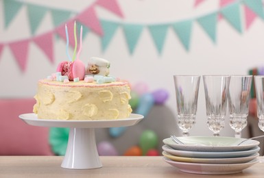Delicious cake decorated with macarons and marshmallows and clean tableware on wooden table in festive room
