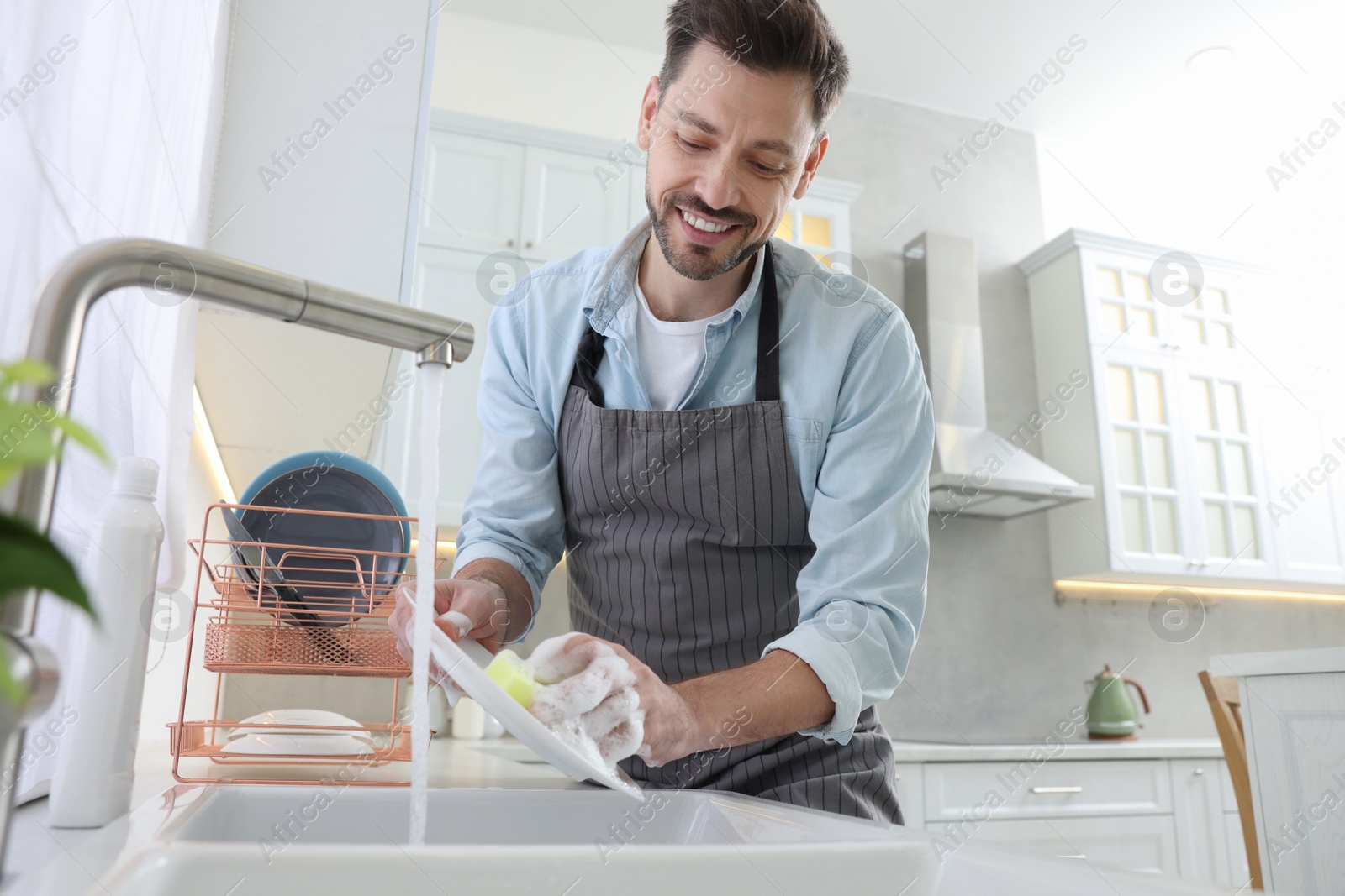 Photo of Man washing plate above sink in kitchen