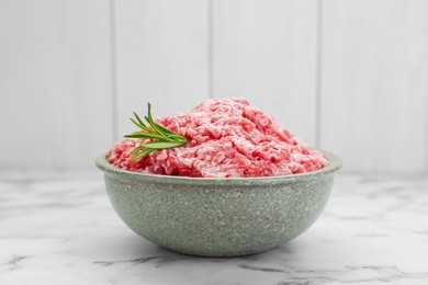 Photo of Bowl of raw fresh minced meat with rosemary on white marble table