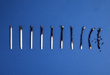 Photo of Different stages of burnt matches on blue background, flat lay