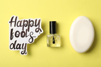 Photo of Soap, transparent nail polish and words Happy Fool's Day on yellow background, flat lay