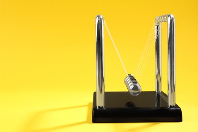 Photo of Newton's cradle on yellow background, space for text. Physics law of energy conservation