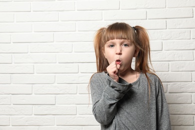 Photo of Cute little girl coughing near brick wall. Space for text