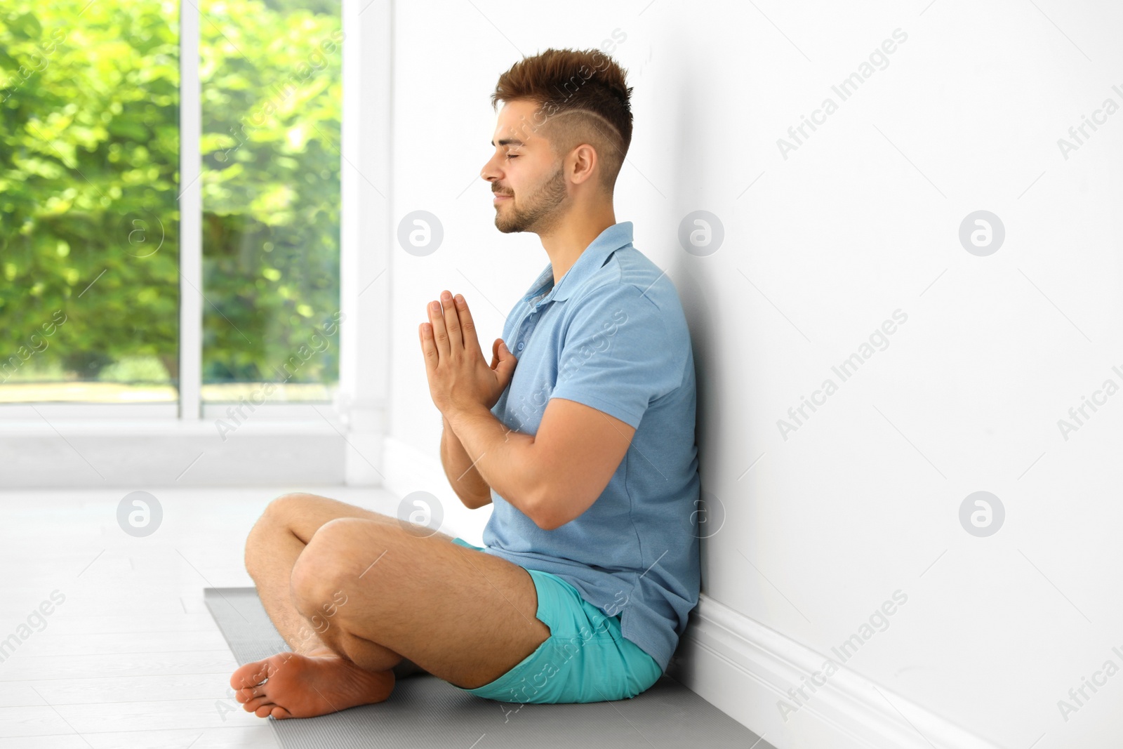 Photo of Young man practicing zen yoga near wall indoors