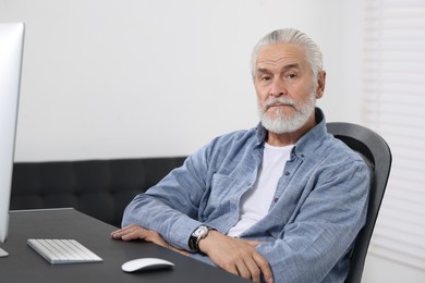 Photo of Handsome senior man working on computer at table in office. Space for text