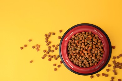 Dry dog food and feeding bowl on orange background, flat lay. Space for text