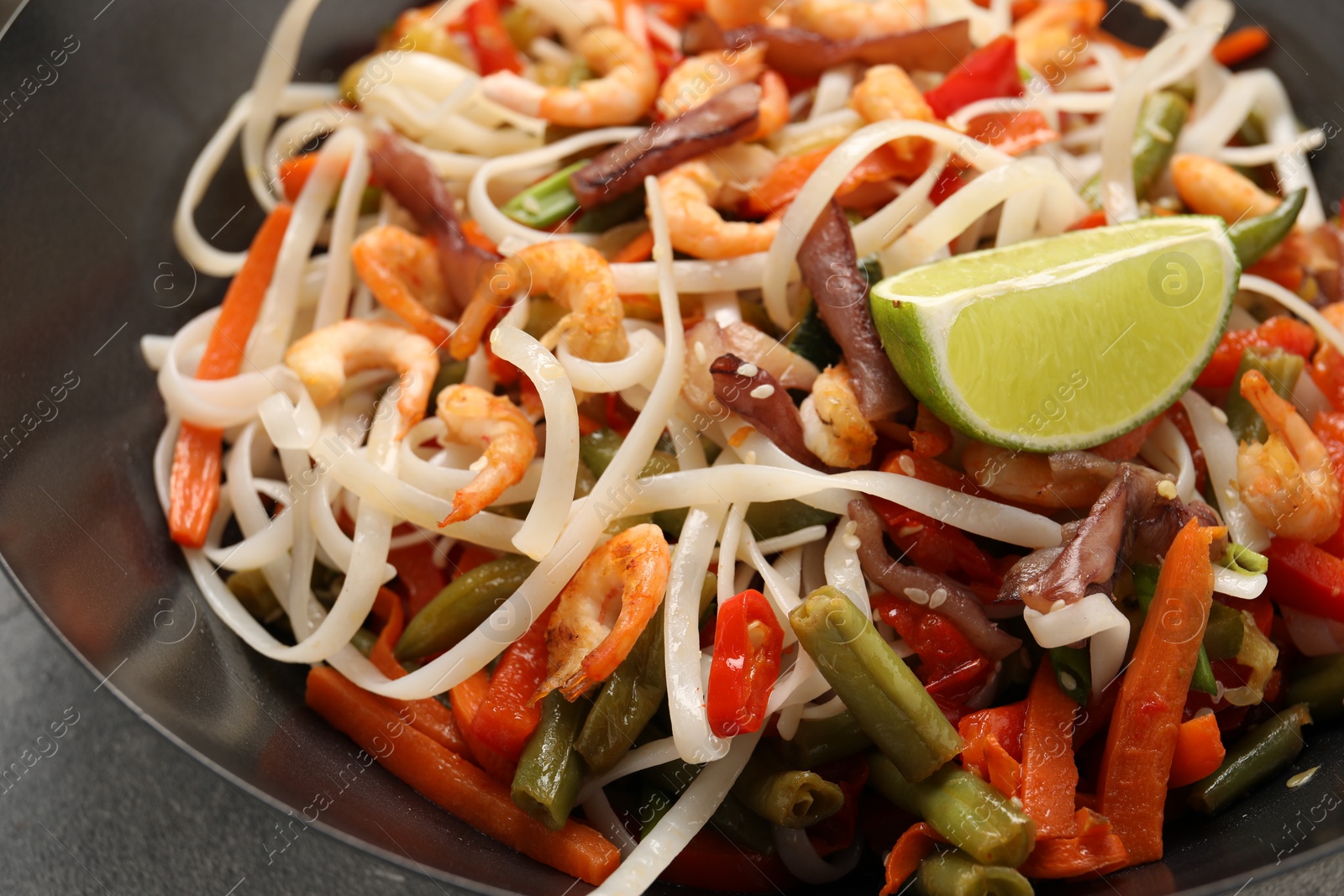 Photo of Shrimp stir fry with noodles and vegetables in wok on grey table, closeup