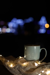 Photo of Cup of hot beverage, sweater and Christmas lights outdoors on winter night