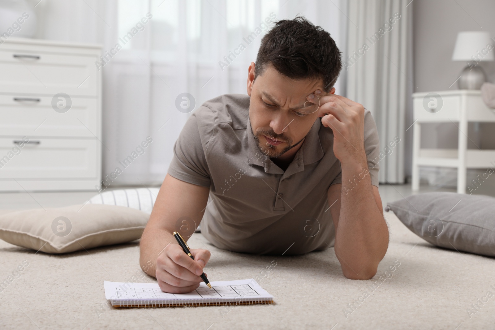 Photo of Man solving sudoku puzzle on floor at home
