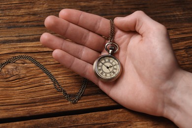 Man holding chain with elegant pocket watch at wooden table, closeup