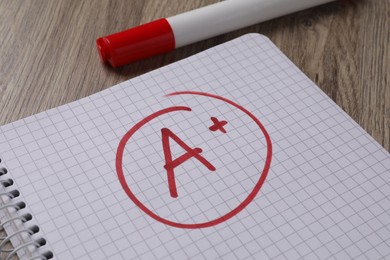 School grade. Red letter A with plus symbol on notebook paper and marker on table, closeup