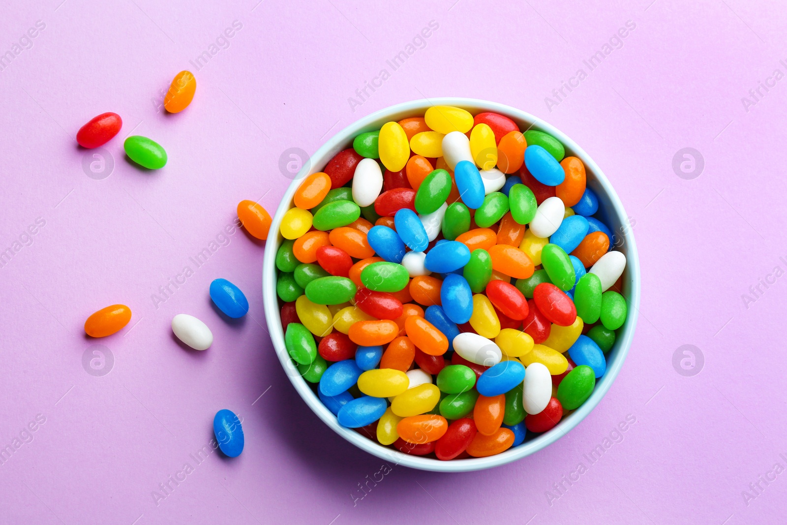 Photo of Bowl with colorful jelly beans on lilac background, flat lay