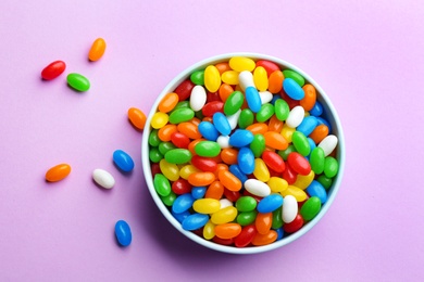 Photo of Bowl with colorful jelly beans on lilac background, flat lay