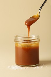 Taking tasty salted caramel with spoon from jar on pale yellow background