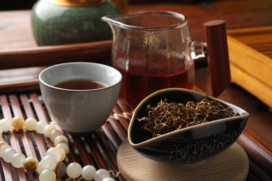 Aromatic Dianhong tea and prayer beads on wooden tray, closeup. Traditional ceremony