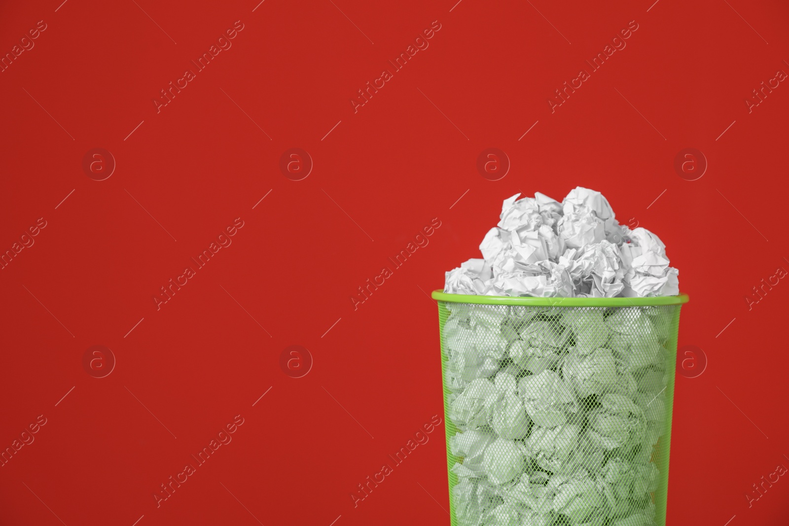 Photo of Metal bin with crumpled paper against color background. Space for text