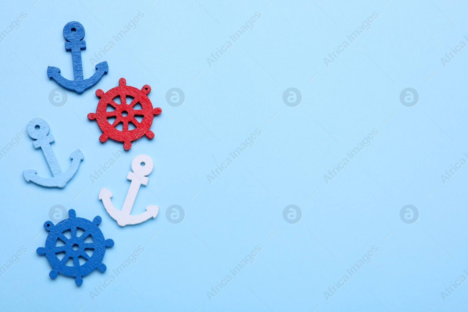 Photo of Anchor and ship wheel figures on pale blue background, flat lay. Space for text